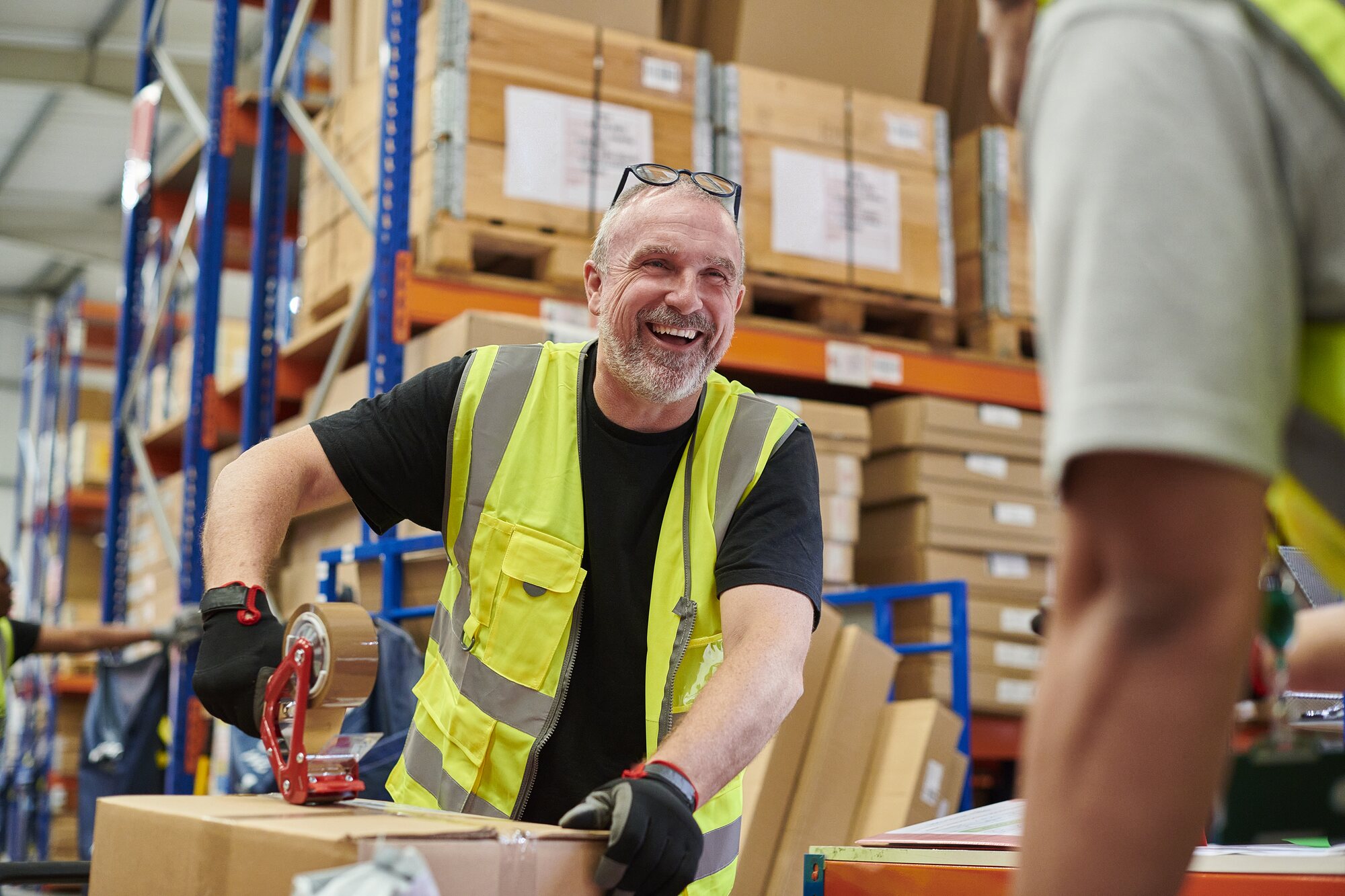A warehouse worker smiling while taping a box on the floor