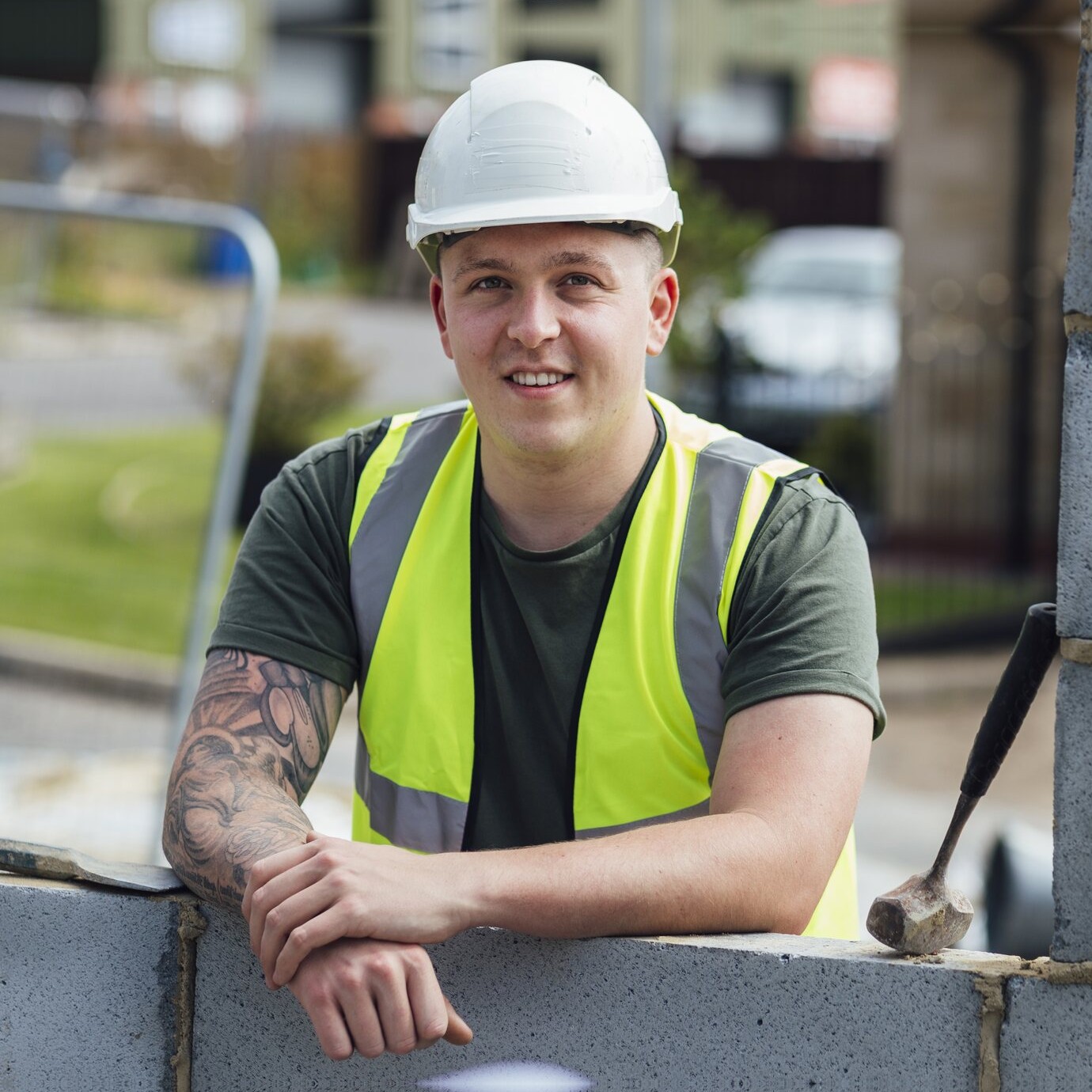 Smiling construction worker in a hard hat leaning on a brick wall on site